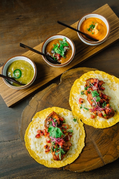 Pollo a la parrilla y tacos de foie gras servidos en una tabla de cortar de madera con diferentes salsas.