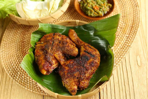 Pollo a la parrilla tradicional indonesio Ayam Bakar Dispuesto en bandeja de bambú con pepino