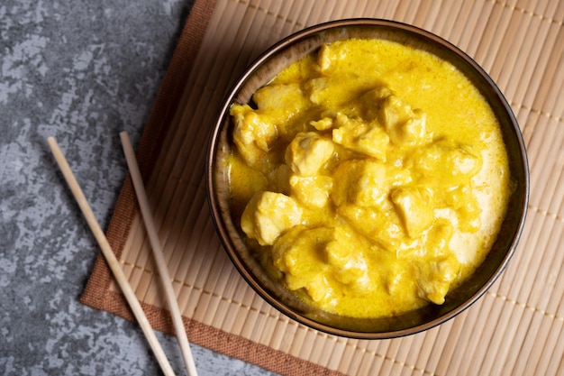 Pollo en salsa de curry en un bol sobre una servilleta de bambú con palillos sobre un fondo gris