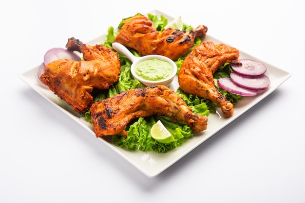 El pollo tandoori es un plato de pollo que se prepara asando pollo marinado en yogur y especias en un tandoor o en un horno de barro, servido con cebolla y chutney verde.