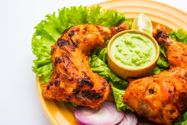 El pollo tandoori es un plato de pollo que se prepara asando pollo marinado en yogur y especias en un tandoor o en un horno de barro, servido con cebolla y chutney verde.