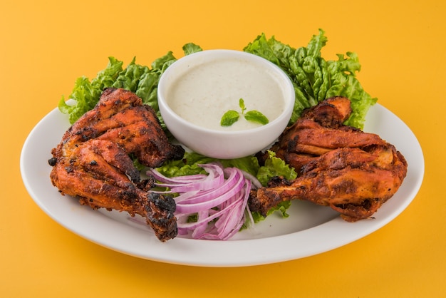 Pollo tandoori: preparado asando pollo marinado en yogur y especias en un tandoor. Pieza de pierna servida en un plato con ensalada sobre fondo de colores o madera. Enfoque selectivo