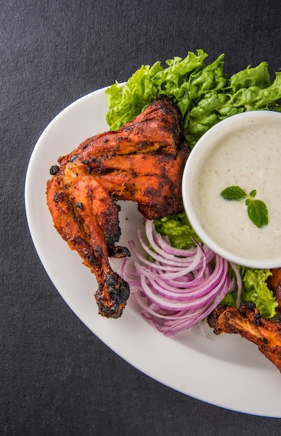 Pollo tandoori: preparado asando pollo marinado en yogur y especias en un tandoor. Pieza de pierna servida en un plato con ensalada sobre fondo de colores o madera. Enfoque selectivo