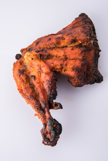 Pollo tandoori: preparado asando pollo marinado en yogur y especias en un tandoor. Pieza de pierna servida en un plato con ensalada sobre fondo de colores o madera. Enfoque selectivo