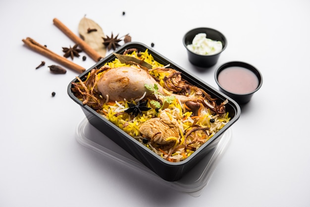 Foto pollo tikka biryani estilo restaurante empacado para entrega a domicilio en caja de plástico o recipiente con raita y salan