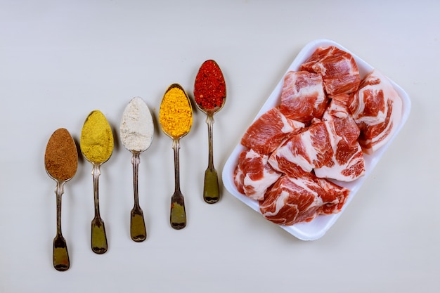 Polpa de carne de porco fresca em um fundo branco de madeira e colheres com diferentes especiarias