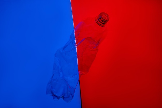 Poluição plástica Aquecimento global Mudança climática Gerenciamento de resíduos Garrafa vazia esmagada usada flutuando em contraste azul vermelho brilhante cópia espaço fundo de arte