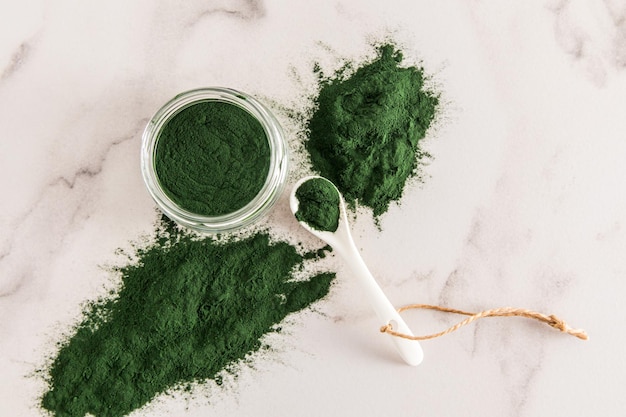 Polvo de algas de espirulina verde orgánico en un frasco grande de vidrio sobre una mesa de mármol, suplementos de vista superior para promover la salud