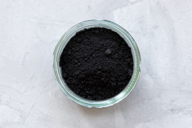 Polvo de carbón activado negro en un vaso. Superalimento, ingrediente para cosméticos y vegano, comida vegetariana, concepto de desintoxicación. Pared gris. Copia espacio, enfoque selectivo