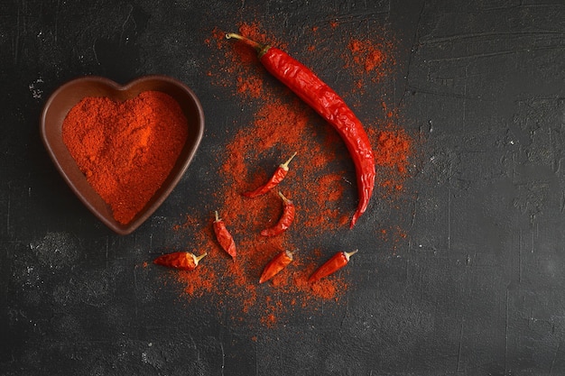 El polvo de chile rojo caliente en un cuenco en forma de corazón en una mesa de piedra negra concepto de amor