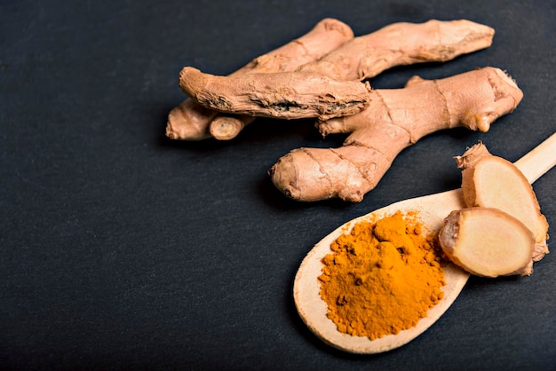 Polvo de curcumina de cúrcuma de primer plano en cuchara de madera con rizoma fresco sobre fondo de madera