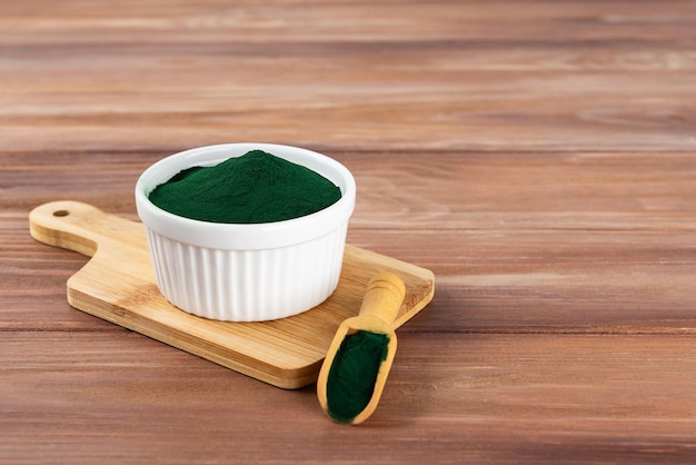 Polvo de espirulina en un bol y una cuchara en una tabla de madera Espacio de copia de orientación horizontal