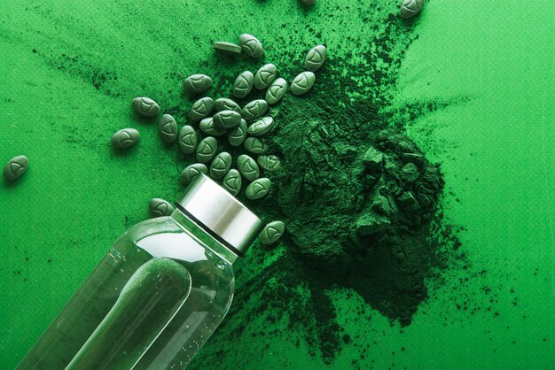 polvo de espirulina y tabletas sobre fondo verde con botella de agua