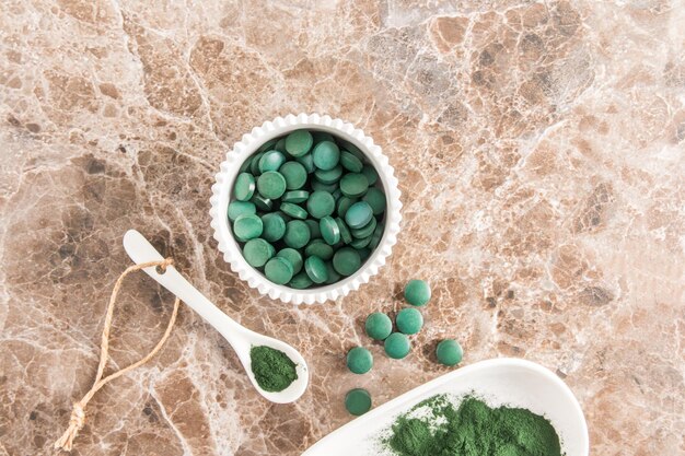 Polvo de espirulina verde orgánico y tabletas de algas verdes en un tazón blanco y una cuchara en una mesa de mármol vista superior fuente de alimento de proteína de vitamina