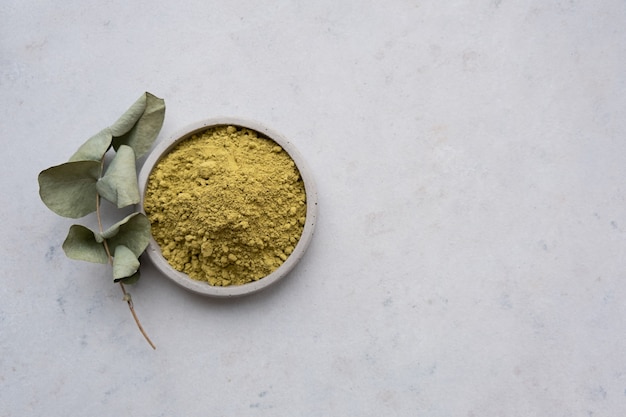 polvo de henna para teñir el cabello y las cejas y dibujar mehendi en las manos sobre un pedestal de cemento gris con flores secas o una flor blanca.