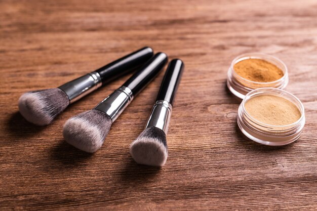 Polvo mineral compacto suelto para rostro y pinceles para polvo y rostro sobre fondo de madera eco