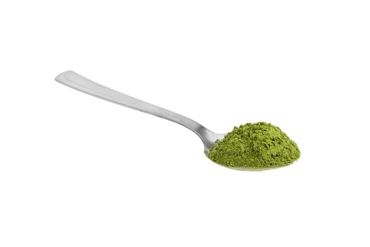 Polvo de pasto de trigo orgánico en cuchara de té de acero aislado en blanco. Superalimento detox.