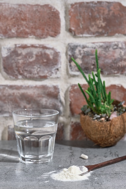 Polvo de proteína de colágeno: hidrolizado, en una cuchara de madera sobre una mesa de piedra, junto a un vaso de agua.