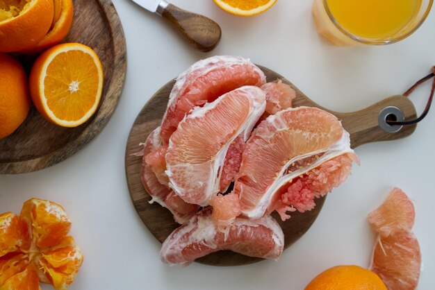 Pomelo em um corte em um suporte de madeira perto de um copo de suco espremido na hora e laranjas