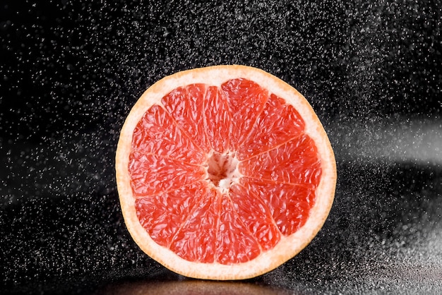 Pomelo con gotas de agua sobre superficie negra