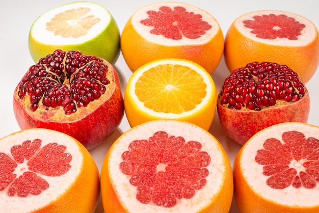 Pomelo jugoso, naranja, granada, cariño cítrico sobre fondo blanco.