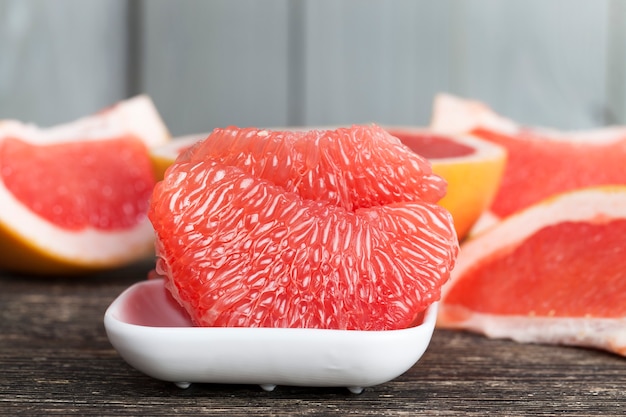 Pomelo rojo pelado roto en rodajas y fibras, acercamiento de jugosos frutos cítricos en un recipiente blanco, preparando un postre