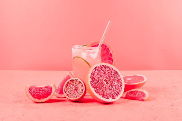 Foto pomelos a la mitad y vaso de jugo sobre fondo coral