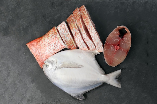 Pomfret branco cavala espanhola peixe pargo limpo pedaços de filé fatiado descamado descamado em fundo de ardósia de mármore preto