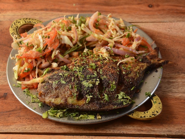 Pomfret peixe tawa frito que é bem guarnecido com tomate repolho limão e cebola servido em fundo de madeira foco seletivo