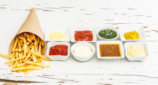 Pommes Frites auf einem Stück Bastelpapier mit verschiedenen Saucen in weißen Bratwürsten auf dem weißen Holz