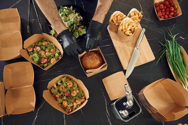 Foto pommes frites, gemüse und burger der mann packt essen in die öko-papierkisten des restaurants.