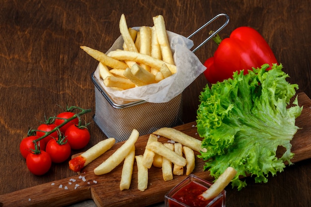 Pommes-Frites in einem Gitter mit Ketchup-, Salat- und Kirschtomaten auf hölzerner brauner Tabelle