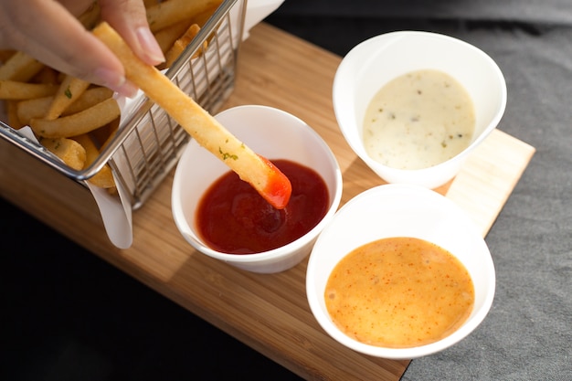 Pommes-Frites in einem Metallkorb mit Soße auf einem Bretterboden.