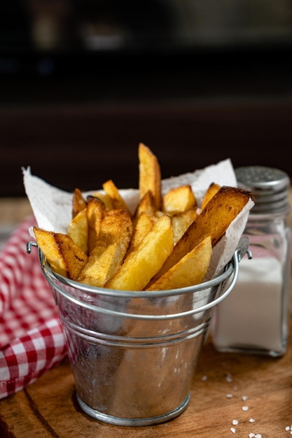 Pommes Frites in einem Metalltopf mit Aioli und Ketchup auf einem Holzbrett Exemplar mit vertikaler Ausrichtung