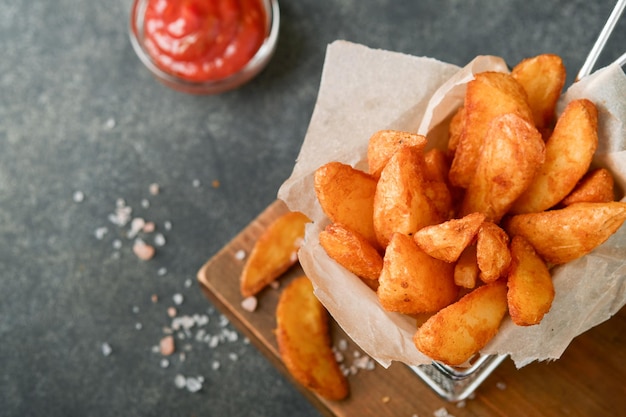 Pommes Frites in Metalldrahtkorb mit Salz und Ketchup auf altem dunklem Holzhintergrund clous up Bratkartoffeln Fast Food und ungesundes Lebensmittelkonzept