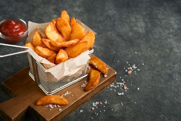 Pommes Frites in Metalldrahtkorb mit Salz und Ketchup auf altem dunklem Holzhintergrund clous up Bratkartoffeln Fast Food und ungesundes Lebensmittelkonzept