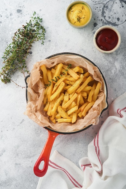 Pommes Frites Leckerer Pommes-Server in roter Gusseisenpfanne mit Tomaten-Käse-Sauce auf altem grauem Betontischhintergrund Diverse Keto-Gerichte Fast Food und ungesundes Food-Konzept