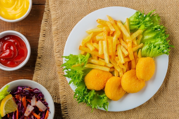 Pommes frites mit Chicken Nuggets in der Nähe von Saucen auf einer Serviette auf einem Holztisch. Horizontales Foto