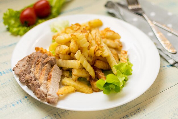 Pommes Frites mit Fleisch auf einem weißen Teller auf hellem Holzhintergrund