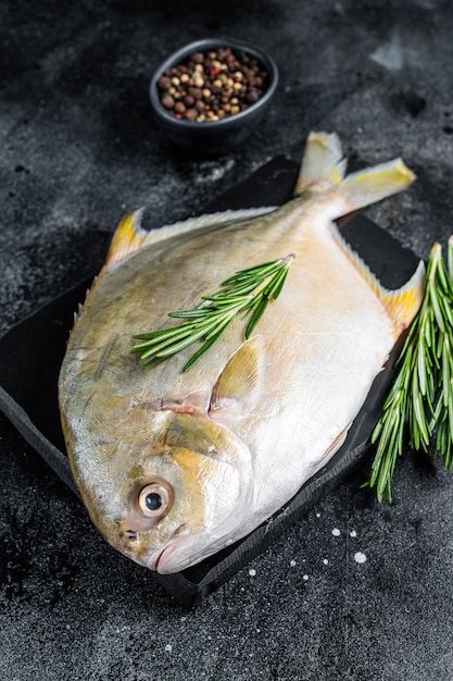 Pompano de pescado crudo con hierbas sobre una placa de mármol