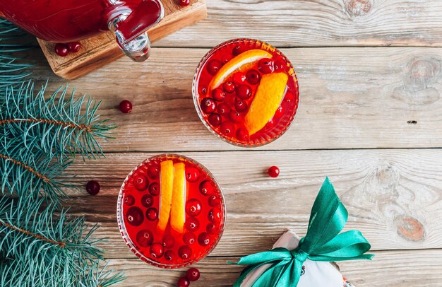 Ponche de arándanos de Navidad con naranjas en una jarra y vasos en una mesa de madera rústica