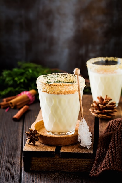 Ponche de huevo Batido de bebida tradicional de Navidad con canela en la mesa vieja oscura.