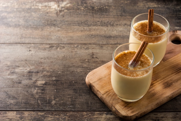 Ponche de huevo casero con canela en vidrio en la mesa de madera, postre típico de Navidad.