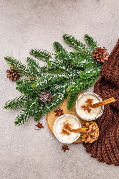 Ponche de huevo casero con canela en vidrio. Postre típico navideño. Brunch de abeto de hoja perenne, conos, cuadros acogedores, nieve artificial.