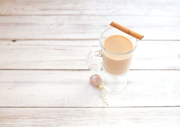 Ponche de huevo de invierno tradicional en taza de vidrio con leche, ron y canela, adornos navideños.