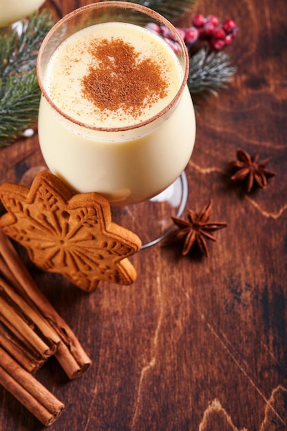 Ponche de huevo de Navidad. Delicioso cóctel de invierno con leche, ron y canela servidos en dos vasos con galletas de azúcar en forma de estrella de mantequilla, rama de abeto sobre una mesa de tablones de madera blanca. De cerca. Bosquejo.