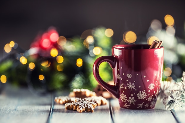 Ponche de Navidad en una taza roja con pan de jengibre, canela y adornos navideños.