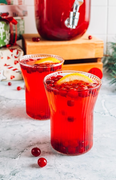 Ponche navideño de arándanos con naranjas en una jarra y vasos sobre una mesa de mármol gris