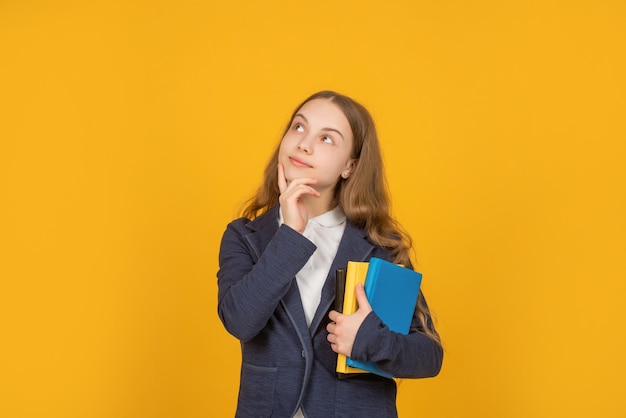 Ponderando a menina adolescente segurar a pasta de trabalho da escola sobre fundo amarelo, lição de casa.
