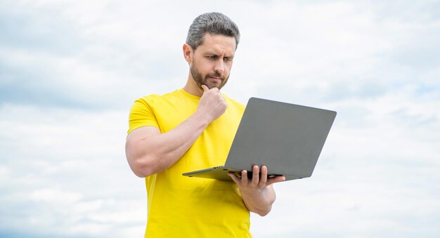 Ponderando o homem trabalhando online no laptop no fundo do céu